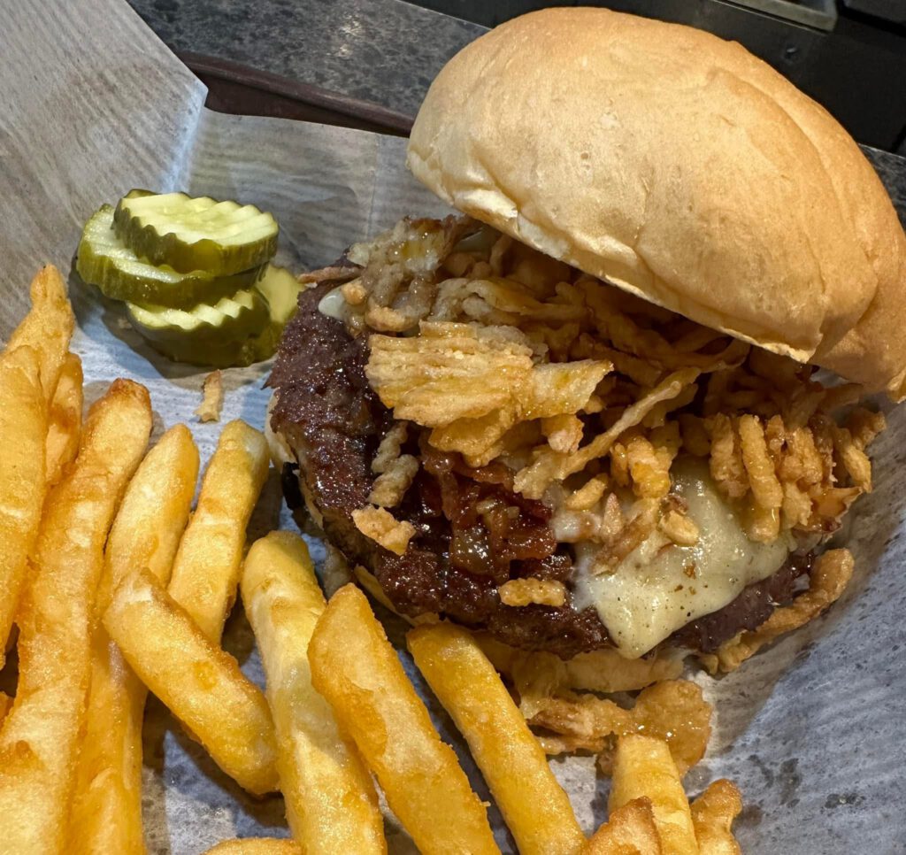 Wrangler Burger with a half-pound beef patty topped with melted cheddar cheese, bacon, BBQ sauce, and crispy fried onions on a toasted bun.