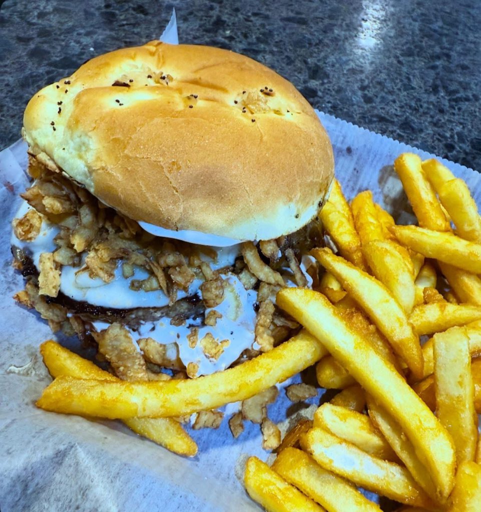 Frenchie Burger with a half-pound beef patty topped with homemade French onion dip, brandied caramelized onions, provolone cheese, and crispy fried onions on an onion roll.